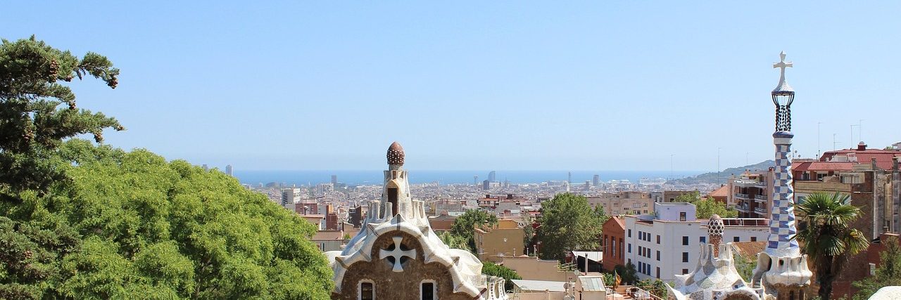 The view from the terrace at Park Guell over Barcelona to the sea, Gaudi's two pavilions with their tiled roofs in the foreground and the city grid stretching beyond.