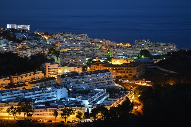Lit white apartment terraces stepping down the hillside at Benalmadena after dark, with the sea beyond.