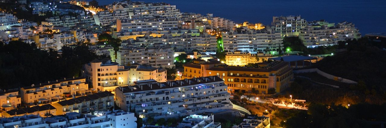 Benalmadena at dusk from above, lit white terraces stepping down a hillside towards a dark sea.