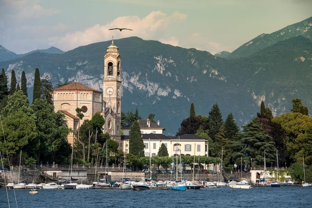 A bell tower and moored boats on the shore of Lake Como.
