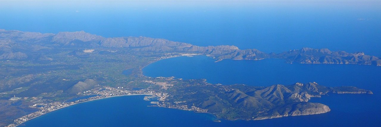 The Bay of Pollenca from the air, the town spread along the flat shore on the left and the long rocky Formentor peninsula closing the bay on the right.
