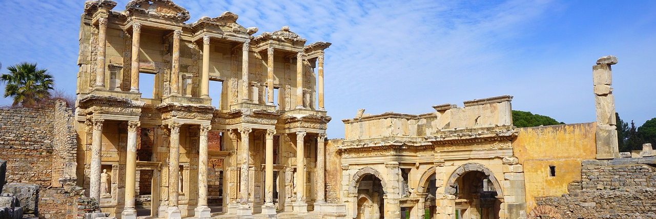 The two-storey columned facade of the Library of Celsus at Ephesus, three kilometres from Selcuk, with the arched gate beside it and a standing column to the right.