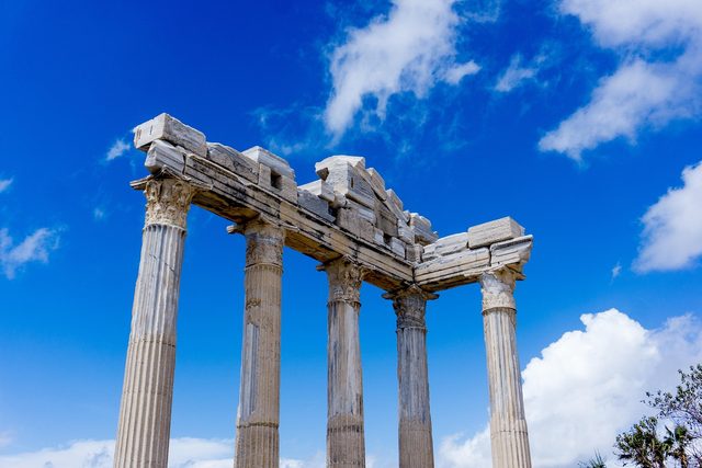 Three columns of the ancient temple at Side against a blue sky.