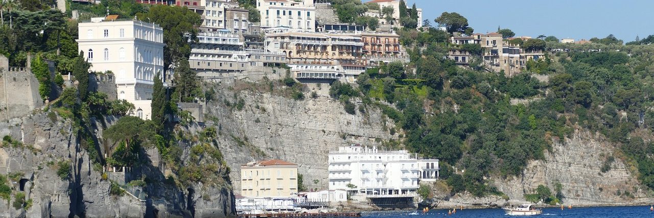 The cliffs at Sorrento with buildings standing along the top and more built down at the water's edge, the sea filling the foreground.