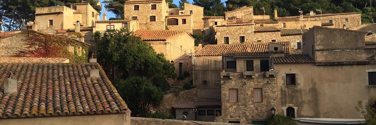 The walled old town of Tossa de Mar on its headland, stone houses and towers rising inside the medieval walls with pines on the slope above.