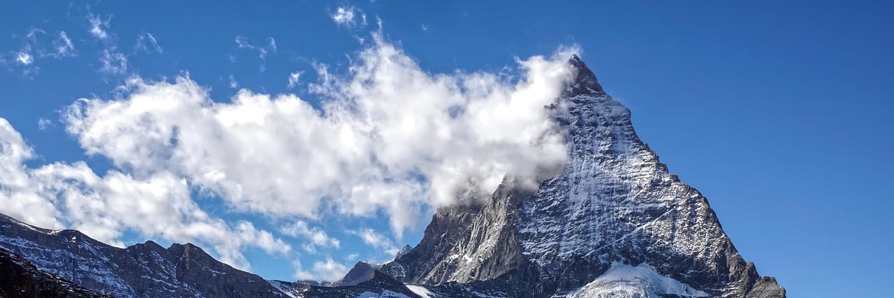 The pyramid of the Matterhorn above Zermatt, snow lying on its faces and cloud along the ridge, dark rock and snowfields below.